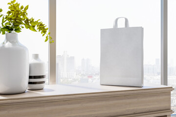 Wall Mural - Sunny city view from room with light vases on light wooden surface and blank white paper bag. Mockup