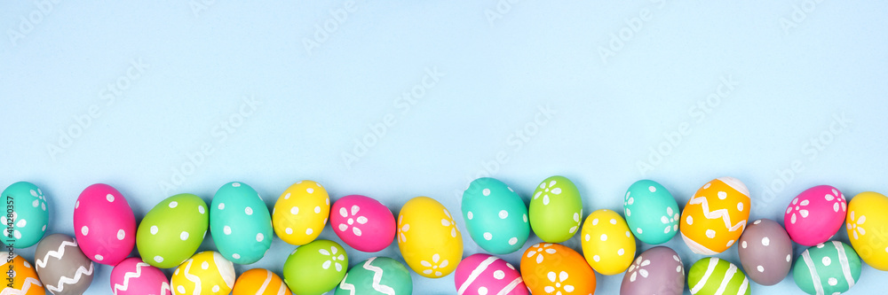 Colorful Easter Egg bottom border over a pastel blue paper banner background. Copy space. - obrazy, fototapety, plakaty 