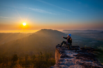 Asian tourist man sits and admires the sunrise on the cliff at Phu Dan Tong,Pho Sai district,Ubon ratchathani province,Thailand.