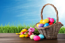 Colorful Easter Eggs In Wicker Basket And Spring Tulips On Wooden Table Outdoors, Space For Text
