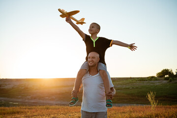 Wall Mural - Dad holds his son around his neck at sunset in the summer they launch a plane against the background of the sky