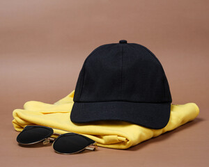 Wall Mural - Blank baseball caps are used for design mockups. The hat on the side of an old camera and sunglasses. Plain hat isolated on brown background. Take a picture of a hat ready to be displayed. Mockup hat.