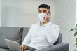 © fotofabrika - Handsome man businessman in medical mask using his laptop while talking on his cellphone