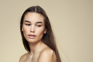 Brunette with bare shoulders close-up long hair beige background clean skin