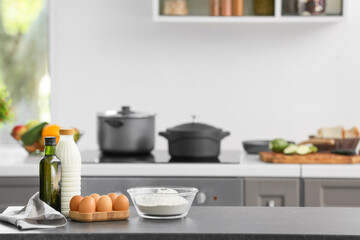 Bowl with flour, eggs and bottle of milk on table in modern kitchen