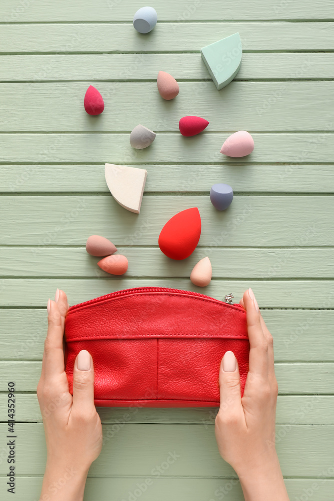 Hands with cosmetic bag and makeup sponges on wooden background