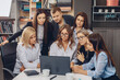 © Semachkovsky  - Seven attractive concentrated office workers sitting at a white table and looking at the monitor of a girl typing on a laptop. Attentive workers. Discussion process. Progress concept
