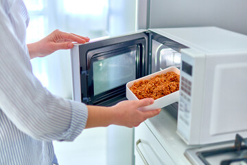 Female hands warming up a container of food in the modern microwave oven for snack lunch at home