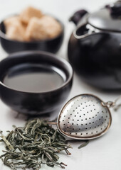 Fresh organic loose green tea with strainer infuser and black teapot and cane sugar on white background.