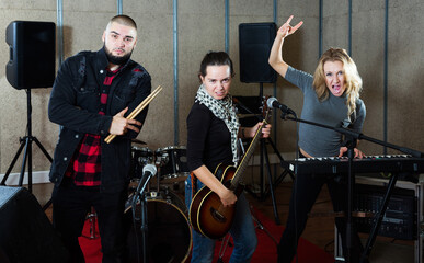 Expressive active group of rock musicians posing with instruments in recording studio