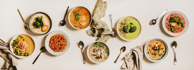 Flat-lay of vegetarian creamy homemade soup and spoons over white plain table background, top view. Autumn and Winter creamy vegan soups, fall and winter vegetarian food menu concept