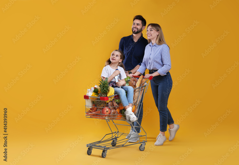 Happy family with shopping cart full of groceries on yellow background - obrazy, fototapety, plakaty 