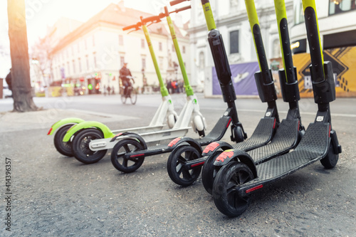 Obraz Dibond Many modern electric kick scooters sharing parked on city street. Self-service stree transport rental service. Rent urban mobility vehicle with smartphone application. Zero emission green eco energy.