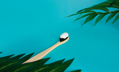 Bamboo toothbrush, toothpaste on a blue background and palm leaves. Oral care concept. copy space for text. top view