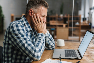 Wall Mural - Tired grey man working with laptop while sitting in office