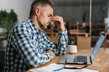 Wall Mural - Unhappy grey man with headache working with laptop in office