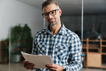 Wall Mural - Joyful white-haired man working with papers while standing in office