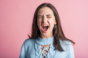 Wall Mural - Portrait of a brunette girl who screams after a quarrel in the studio on a pink background