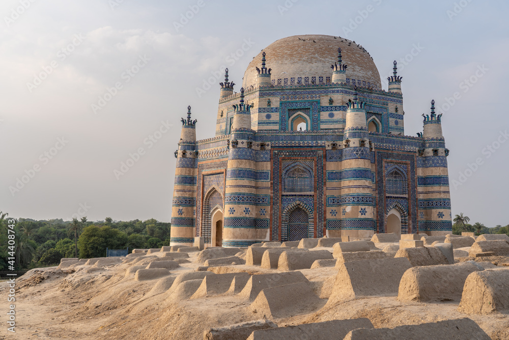 Landscape sunset view of beautiful ancient medieval blue tomb of Bibi Jawindi with traditional graveyard in foreground in Uch Sharif, Bahawalpur, Punjab, Pakistan - obrazy, fototapety, plakaty 