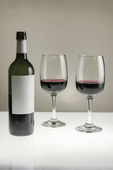 Vertical shot. Two glasses and a bottle of red wine on a blurred homogeneous background. 