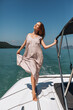 © Semachkovsky  - Full-length portrait. Leggy beauty with a charming smile wearing a long gray dress posing on a white boat and enjoying the sunshine falling on her face. Concept of happiness