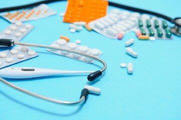 Wall Mural - Scattered white pills on blue table.Medical, pharmacy and healthcare concept. Blue background white pills with a medical statoscope, top view.