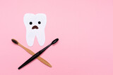 Fototapeta  - Care for the oral cavity. A startled tooth, cut out of felt with crossed toothbrushes, in the shape of a skull and bones. Flat lay. Pink background. Copy space. The concept of dental diseases