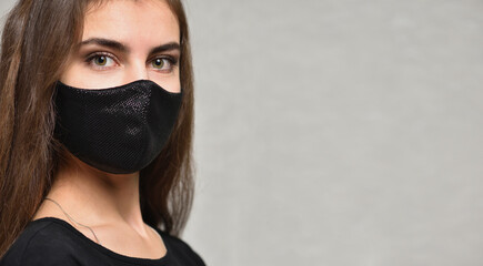 Close up face of young woman in protective black face mask on gray background