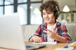 © Friends Stock - Get more knowledge. Happy latin american little boy wearing headphones, looking at the screen of a laptop while communicating with his teacher during online lesson at home