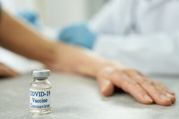 Old woman hand resting on the table with COVID-19 vaccine