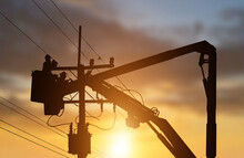 Silhouette Electrician Works On Bucket Car To Maintain High Voltage Transmission Line On Sunset Background