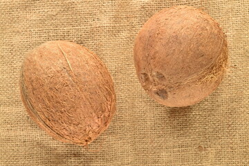 Two ripe organic coconuts on burlap, close-up, top view.