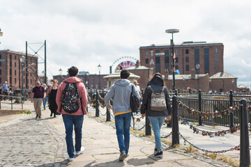 three tourists friends on their back with backpacks walking in the Royal Albert Dock of Liverpool