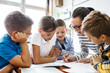 © BalanceFormCreative - Female teacher helps school kids to finish they lesson.They sitting all together at one desk.