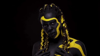 Wall Mural - Face art. Dancing woman with black and yellow body paint. Young african girl with colorful bodypaint. An amazing afro american model with yellow makeup. Closeup face.
