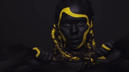 Wall Mural - Face art. Woman with black and yellow body paint. Young african girl with colorful bodypaint. An amazing afro american model with yellow makeup.