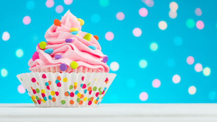 Wall Mural - Happy Birthday cupcake. Tasty cupcakes with pink cream icing and colored sprinkles. Sweet delicious dessert on white wooden table and blue background with bokeh. Copy space. 