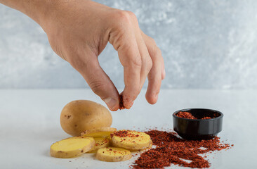 Wall Mural - Man pours chili pepper on sliced potato