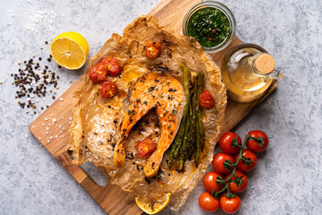 Wall Mural - baked salmon steak on parchment with vegetables, asparagus, tomatoes on a gray background