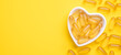 Omega 3 capsules in a heart-shaped plate on yellow background. Fish oil softgels. Supplement food vitamin D capsules. Copy space - Image