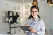 © amnaj - Asian young woman. Looking at camera holding a tablet at the office.