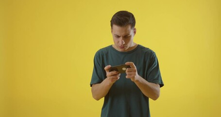 Wall Mural - young man with mobile phone playing game on color background