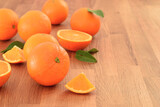 Fototapeta Kuchnia - Ripe fresh raw orange citrus fruit on wooden table. Cut off parts and green leaves.