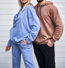 Wall Mural - Blonde girl is standing in blue sport outfit. Man wears brown hoodie and black pants. Couple is wearing street matching outfit