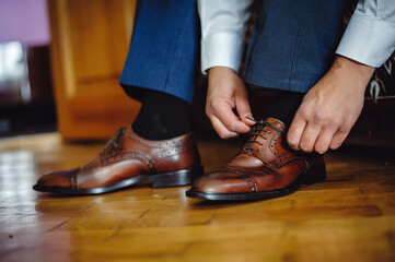 Wall Mural - The groom morning before wedding ceremony wears shoes. Businessman tie the laces on the shoes. Men's style. Professions. To prepare for work, to the meeting.