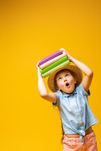 Surprised Child In Straw Hat Holding Books Above Head Isolated On Yellow