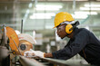 Engineering male african american workers wear soundproof headphones and yellow helmet standing using laptop at iron cutting machine in factory Industrial.