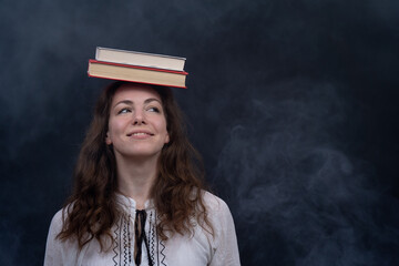 Girl holding books on the head. Concept of genius, meditation and knowledge 