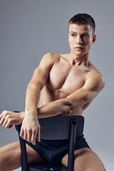 handsome man in black shorts athletic physique sitting on a chair posing