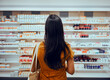 © StratfordProductions - Rear view of young woman with bag standing against shelf in pharmacy searching for medicine